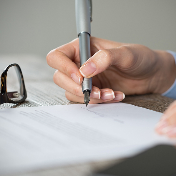Closeup shot of a woman signing a form. Businesswoman signing a new agreement at office. Shallow depth of field with focus on tip of the pen.